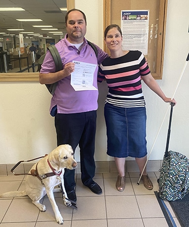 Stpehen, Mary Beth, and their service dog Mae pose at the MVD office. 